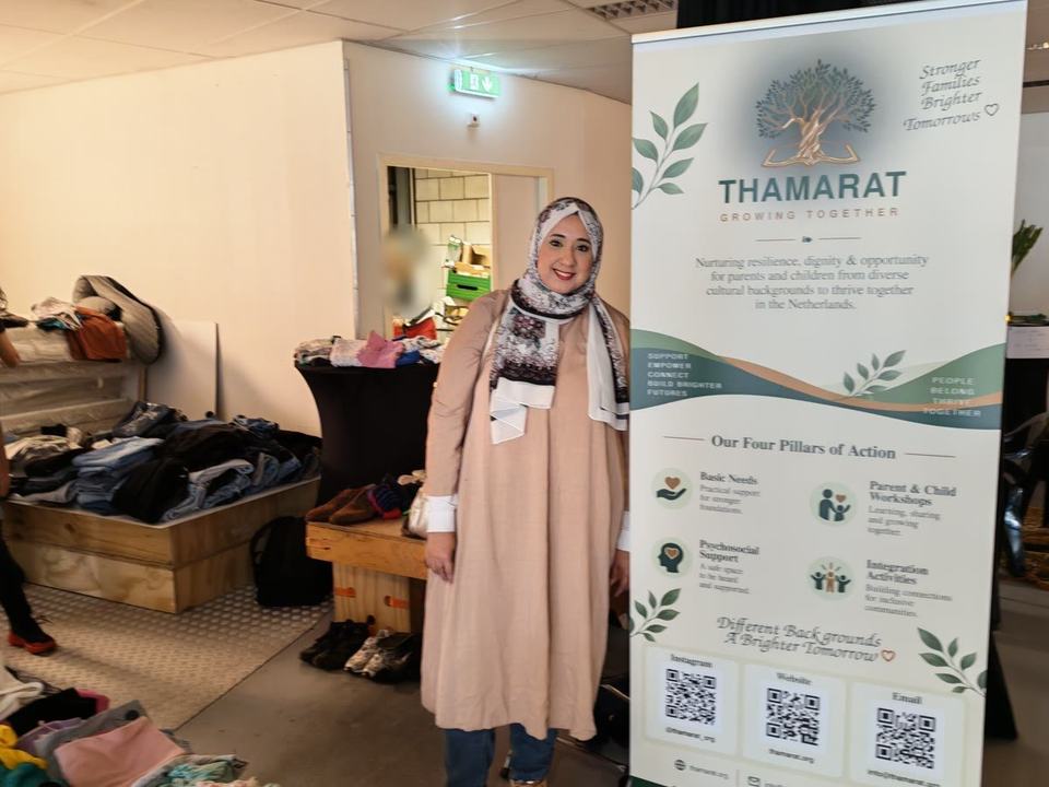 Yara Gamal, de oprichter van Thamarat, naast de banner van Thamarat, met kleding op kratten en de bazaar achter haar.