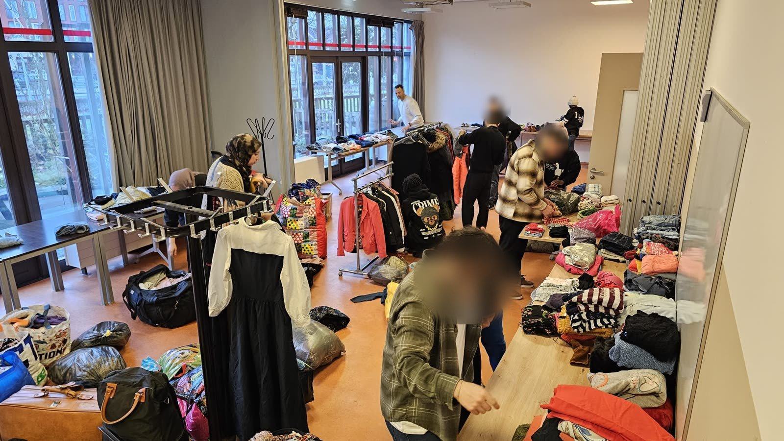 Yara Gamal, our founder, and our co-founder sorting donated clothes onto tables and rails in a community hall with volunteers, with bags of donations on the floor. Some faces are blurred.