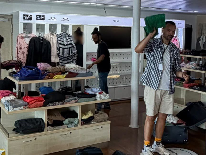 Onze medeoprichter en twee vrijwilligers leggen opgevouwen kleding op schappen en rekken in een winkelruimte aan boord van een schip.